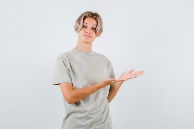 Muchacho adolescente joven que muestra gesto de bienvenida en camiseta y que parece suave. vista frontal.