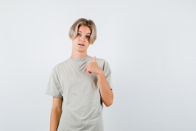 Muchacho adolescente joven que muestra el pulgar hacia arriba en la camiseta y que parece orgulloso, vista frontal.