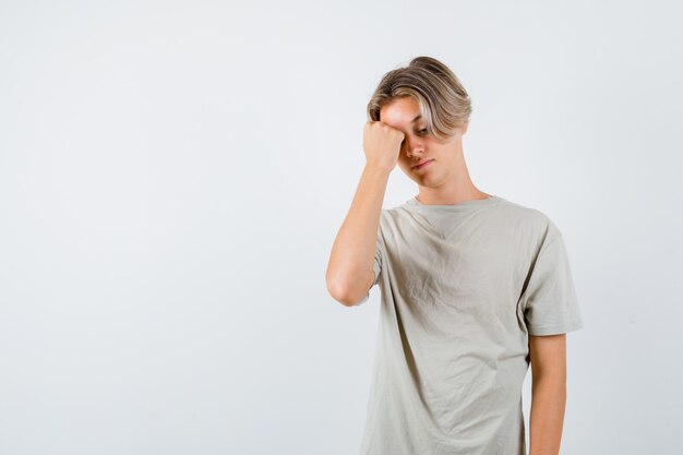 Muchacho adolescente joven que siente dolor de cabeza en camiseta y parece molesto. vista frontal.