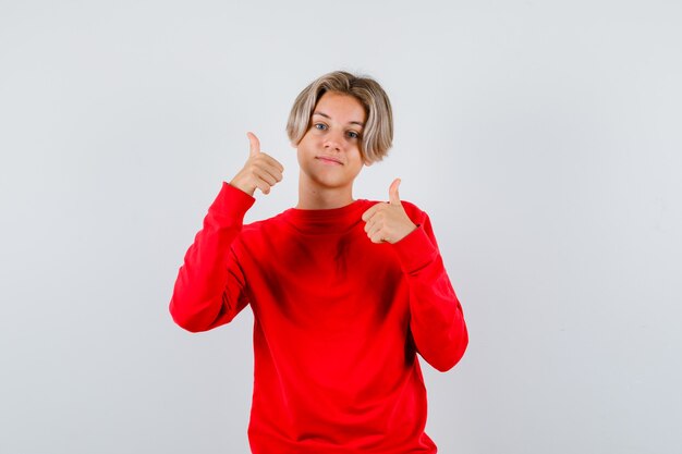 Muchacho adolescente joven en suéter rojo mostrando doble pulgar hacia arriba