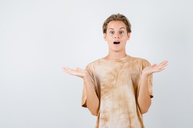 Muchacho adolescente mostrando un gesto de impotencia en camiseta y mirando sorprendido, vista frontal.