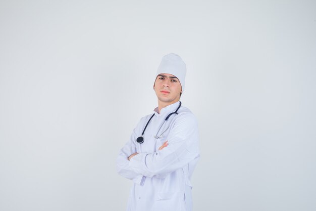 muchacho adolescente de pie con los brazos cruzados en uniforme de médico y mirando confiado