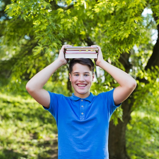 Muchacho adolescente que sostiene los libros en su cabeza