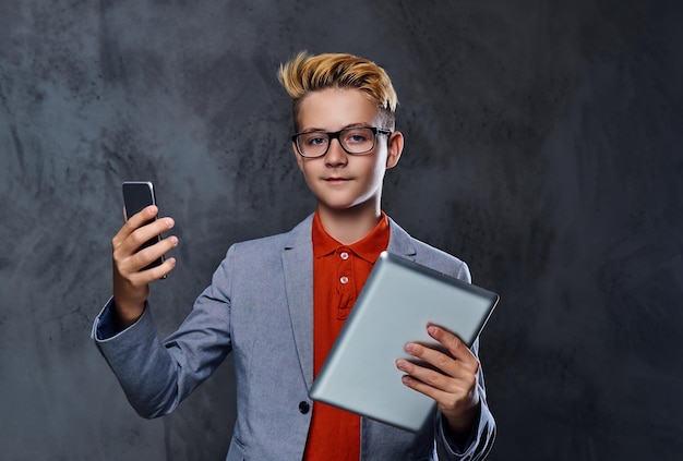 Muchacho adolescente rubio en anteojos tiene tablet PC y smartphone.