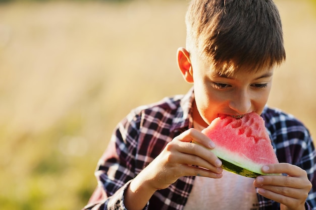 Muchacho adolescente usa camisa a cuadros con aparatos ortopédicos en los dientes come sandía