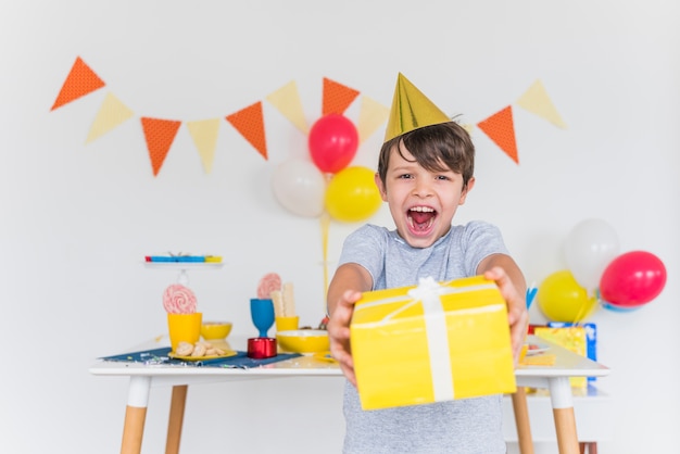 Muchacho alegre que toma la caja de regalo amarilla con la cinta blanca