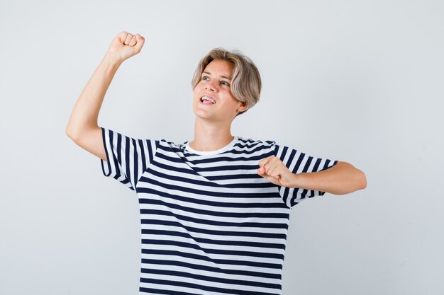 Muchacho bastante adolescente que muestra el gesto del ganador en la camiseta rayada y que parece feliz, vista frontal.