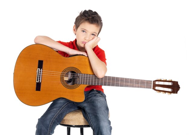 Muchacho blanco triste con una guitarra acústica en sus manos. El niño no quiere participar en la música.