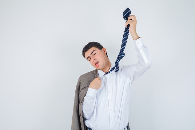 Muchacho en camisa, chaqueta, corbata a rayas haciendo gesto de suicidio con corbata y mirando desesperado