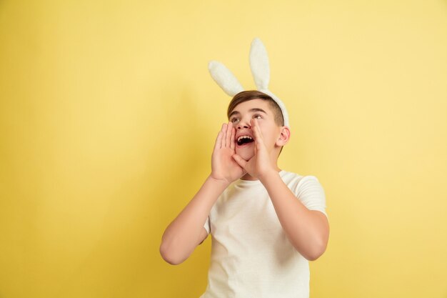 Muchacho caucásico como un conejito de Pascua en el fondo amarillo del estudio. Felices saludos de pascua.