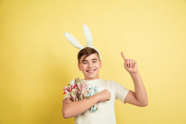 Muchacho caucásico como un conejito de Pascua en el fondo amarillo del estudio.