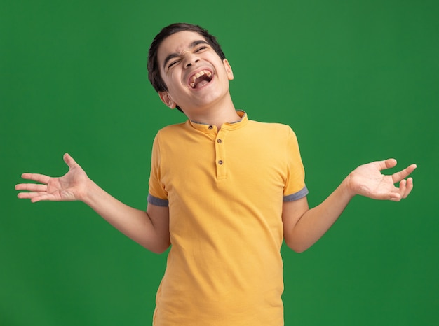 Muchacho caucásico joven estresado que muestra las manos vacías que gritan con los ojos cerrados aislados en la pared verde