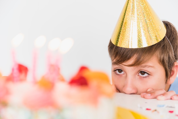 Muchacho de cumpleaños en sombrero de fiesta mirando su pastel