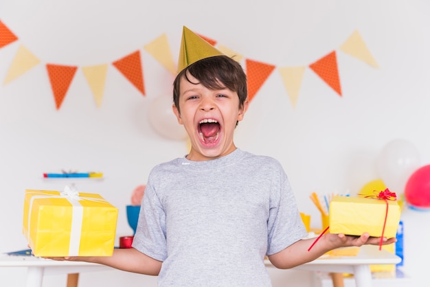 Foto gratuita el muchacho emocionado con es boca abierta que lleva a cabo regalos de cumpleaños en la mano