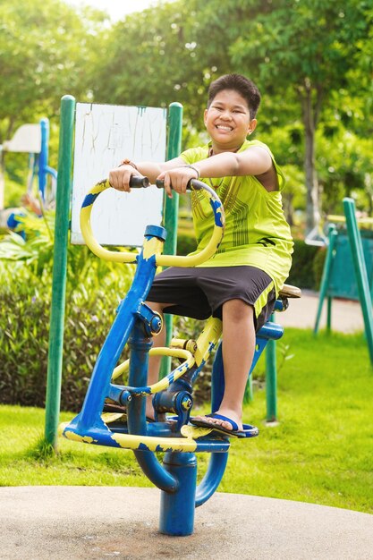 Muchacho feliz del deporte asiático juega en el patio del columpio en el jardín