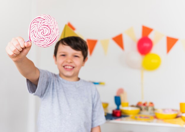 Muchacho feliz que muestra la piruleta dulce del remolino que se coloca en casa