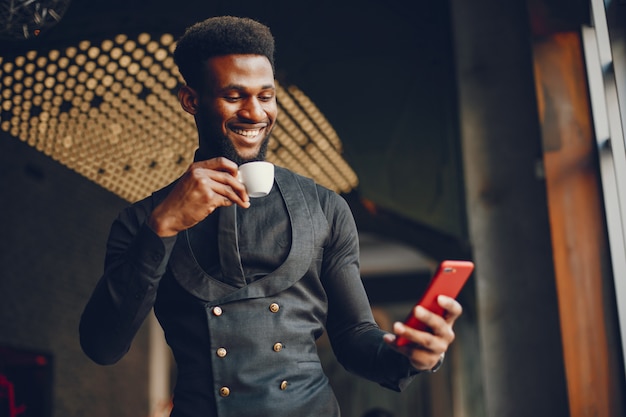 Un muchacho joven y guapo de piel oscura en un traje negro de pie en un café