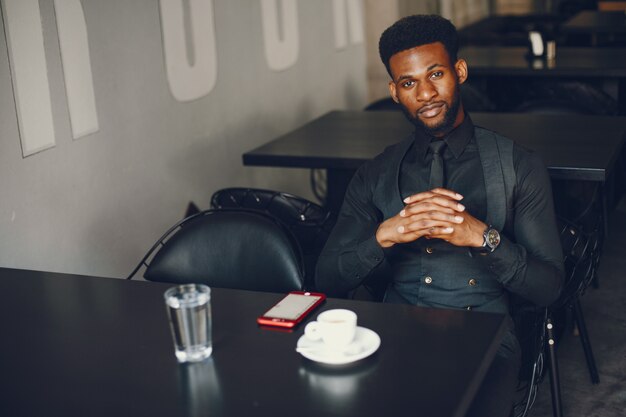 Un muchacho joven y guapo de piel oscura en un traje negro sentado en un café