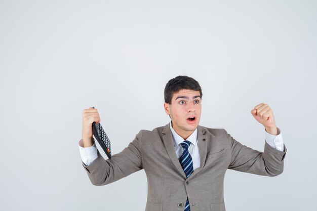 Muchacho joven que sostiene la calculadora, que muestra el gesto del ganador en traje formal