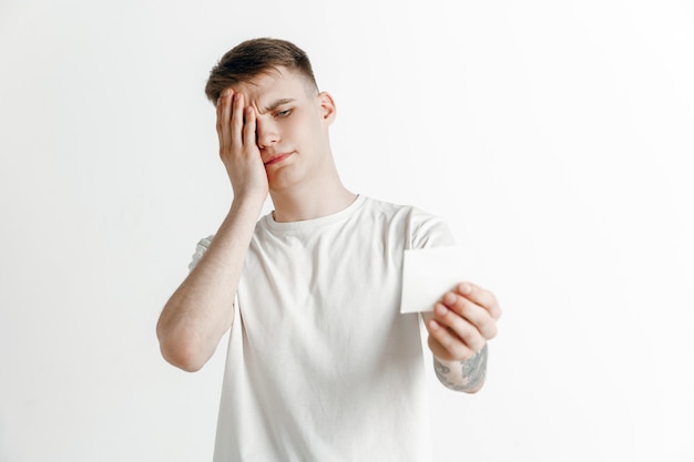 Muchacho joven con un resbalón de apuesta de expresión de fracaso infeliz sorprendido sobre fondo de estudio. Emociones faciales humanas y concepto de apuestas.