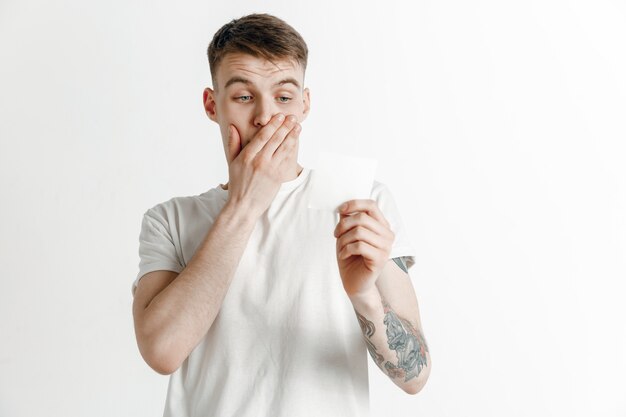 Muchacho joven con un resbalón de apuesta de expresión de fracaso infeliz sorprendido sobre fondo de estudio. Emociones faciales humanas y concepto de apuestas.