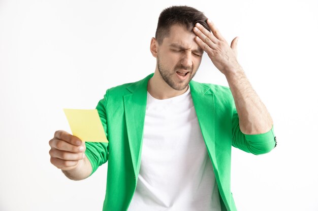 Muchacho joven con un resbalón de apuesta de expresión de fracaso infeliz sorprendido sobre fondo de estudio.