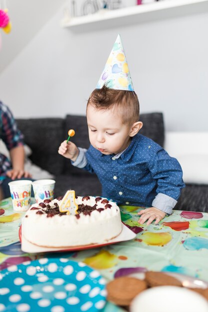 Muchacho lindo que sopla la vela en la torta