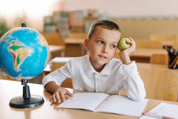 Muchacho con la manzana en el escritorio en escuela