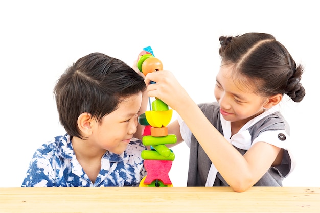 El muchacho y la muchacha asiáticos están jugando feliz el juguete colorido del bloque de madera