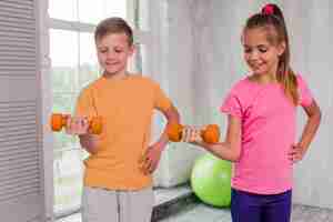 Foto gratuita muchacho y muchacha sonrientes con la mano en las caderas que ejercitan con pesas de gimnasia