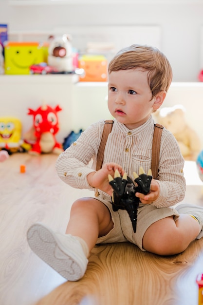 Muchacho que se sienta jugando con el juguete del dinosaurio