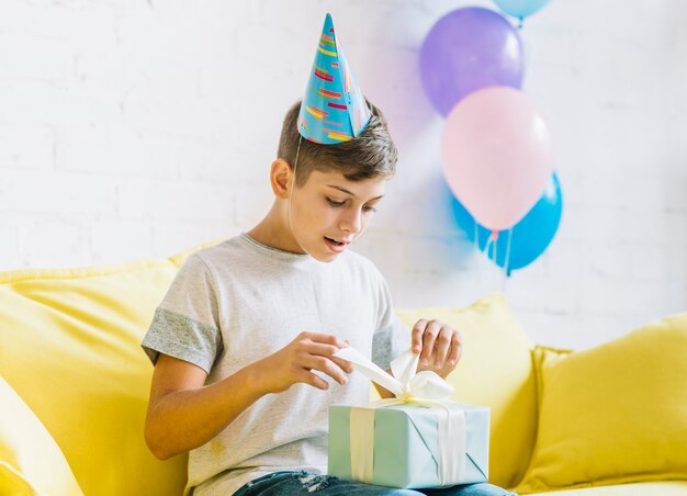 Muchacho que se sienta en el sofá que desempaqueta el regalo de cumpleaños