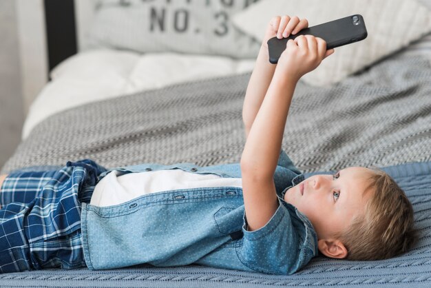 Muchacho rubio que miente en cama usando el teléfono celular