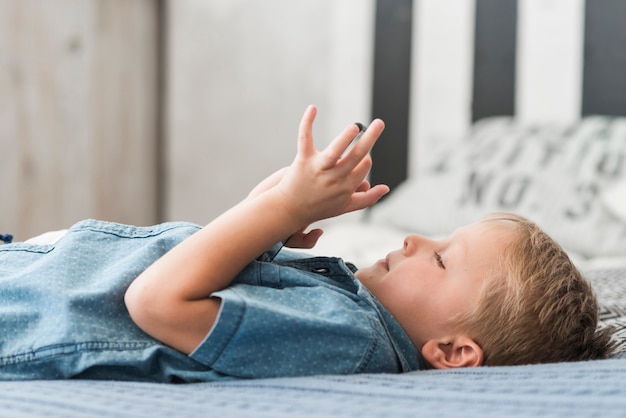 Muchacho rubio que miente en cama usando el teléfono móvil