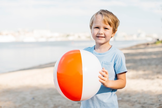 Muchacho sonriente que lleva la pelota de playa