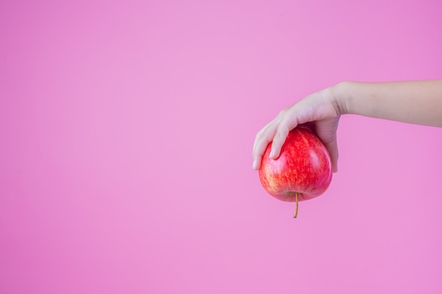 El muchacho sostiene y come manzanas rojas en un fondo rosado.