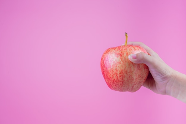 El muchacho sostiene y come manzanas rojas en un fondo rosado.