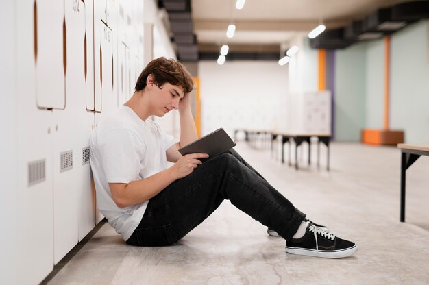 Muchacho de tiro completo leyendo en el piso en la escuela