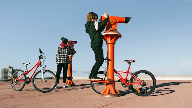 Foto gratuita muchachos con bicicletas mirando a través de telescopios al aire libre