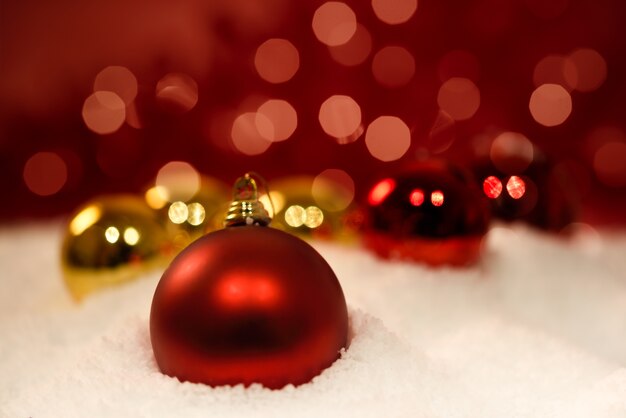 Muchas bolas de navidad en nieve con efecto bokeh y fondo rojo