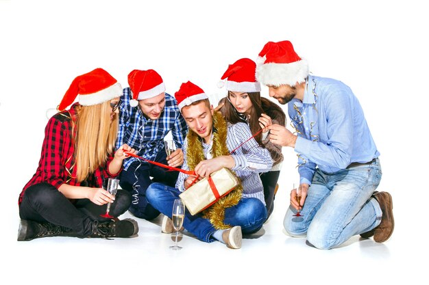 Muchas mujeres y hombres jóvenes bebiendo en la fiesta de Navidad sobre fondo blanco de estudio con regalo