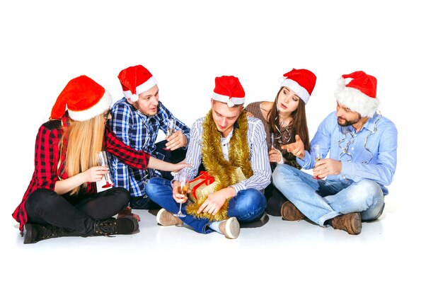 Muchas mujeres y hombres jóvenes bebiendo en la fiesta de Navidad sobre fondo blanco de estudio con regalo