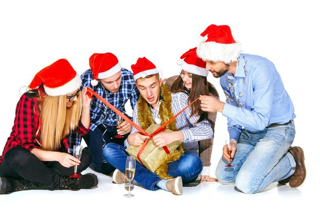 Muchas mujeres y hombres jóvenes bebiendo en la fiesta de Navidad sobre fondo blanco de estudio con regalo