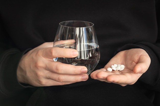 Muchas pastillas blancas y un vaso de agua en manos de un hombre