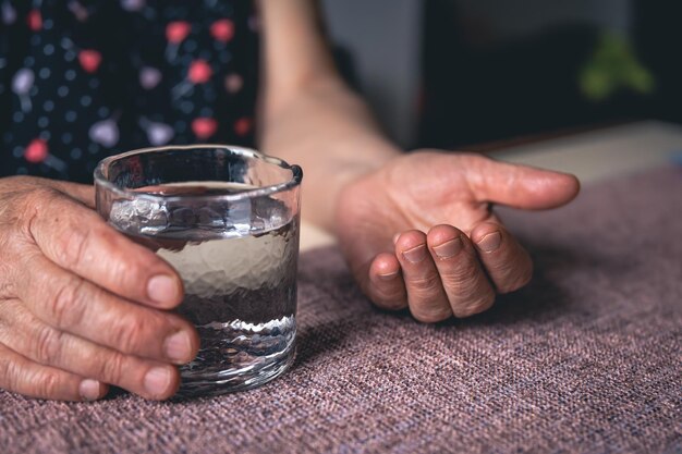 Muchas pastillas y un vaso de agua en manos viejas