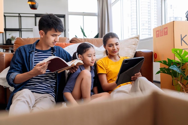 Mudarse a casa concepto familia asiática relajarse tiempo libre sentarse junto con caja de cartón y cosas papá mamá hija pasar tiempo juntos después de terminar de empacar muebles para la mudanza del apartamento