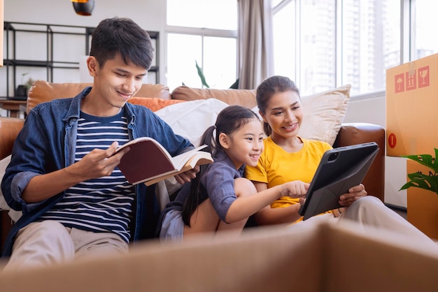 Mudarse a casa concepto familia asiática relajarse tiempo libre sentarse junto con caja de cartón y cosas papá mamá hija pasar tiempo juntos después de terminar de empacar muebles para la mudanza del apartamento