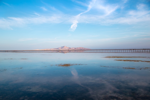 Muelle largo entre mar y montaña. El cielo se refleja en el agua.