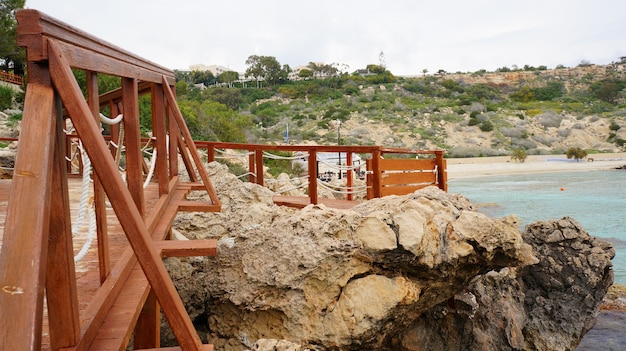 Muelle de madera cerca del océano rodeado de rocas bajo el cielo azul