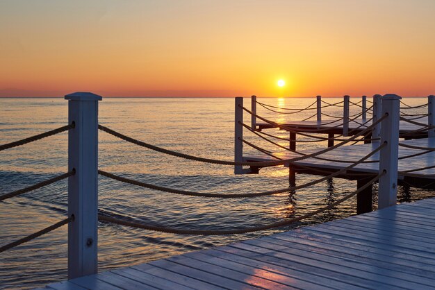 Muelle de madera en una elegante puesta de sol naranja.